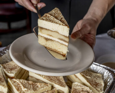 A slice of tiramisu being plated from a catering dish