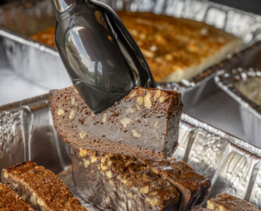 Fudge brownie bars in a catering dish, one slice being lifted by tongs